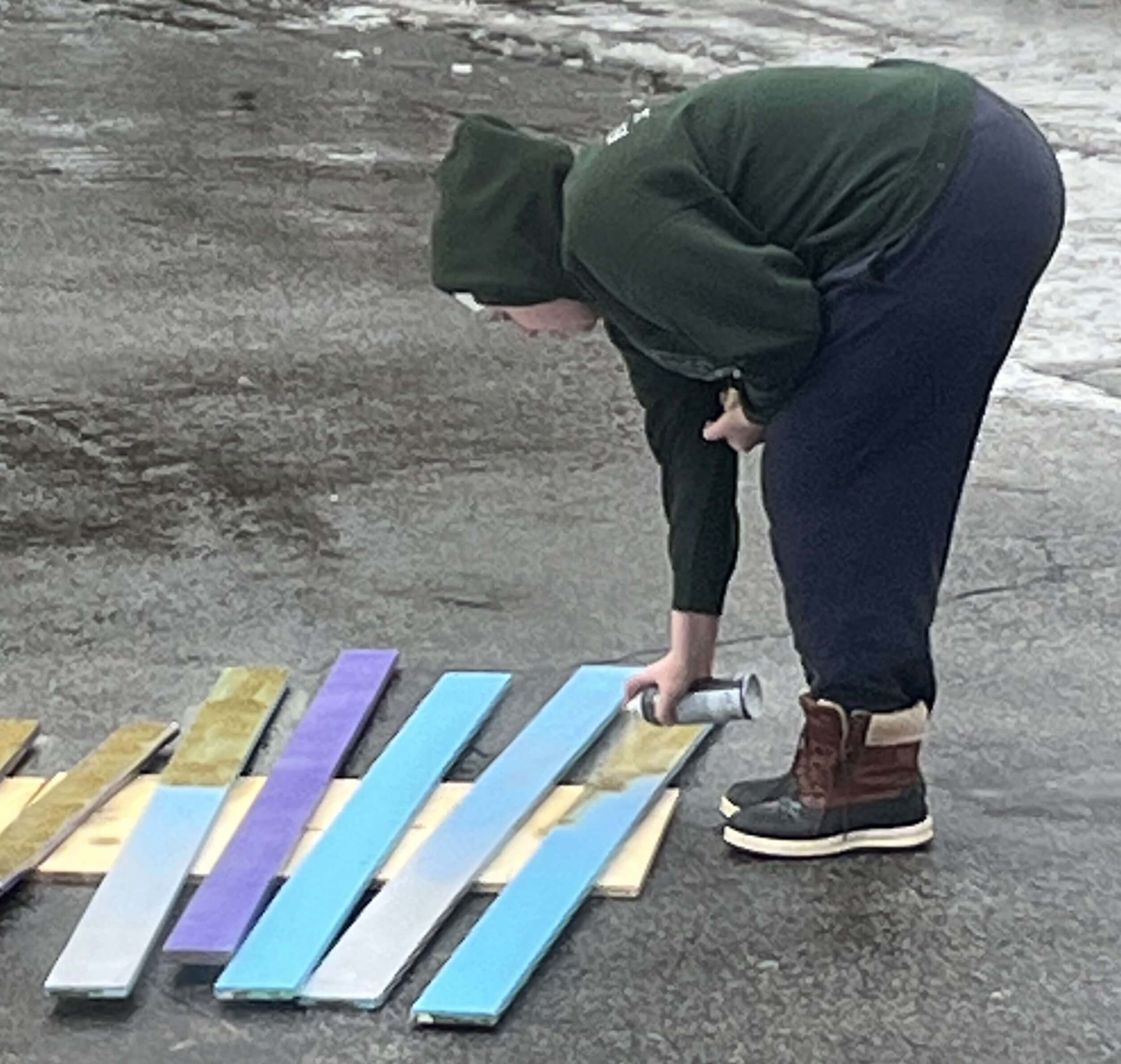 Un membre de l'équipe qui peint à l'aérosol les planches de bois du kiosque.